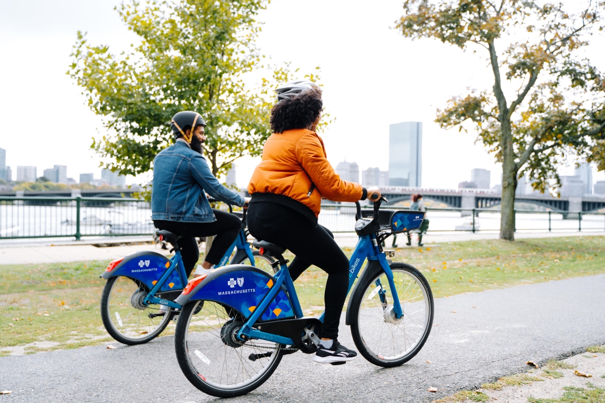 A photo of two people riding bluebikes bikeshare bikes on the esplanade in Boston. 